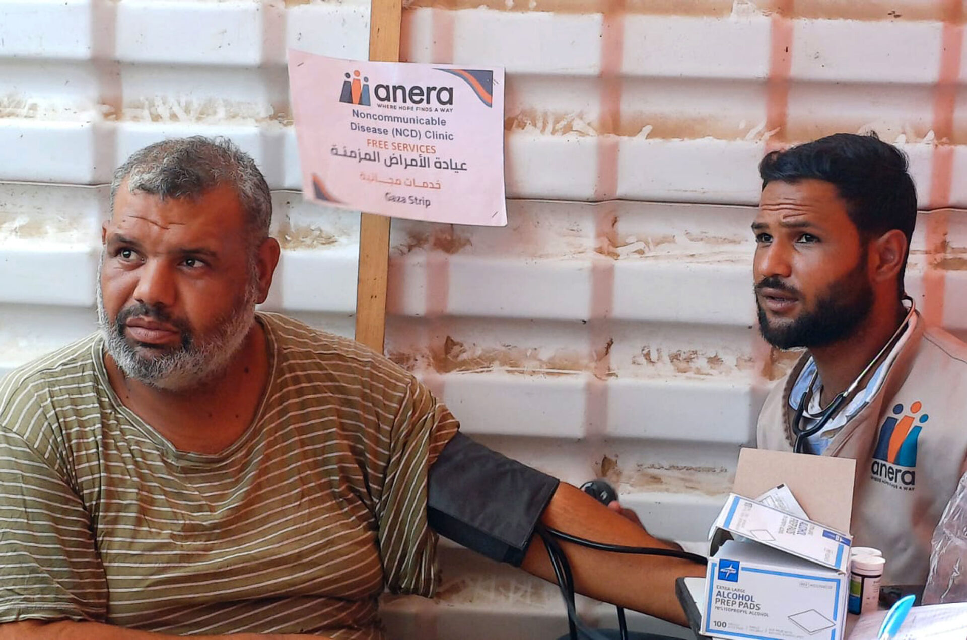 A man sits in front of a wall while his blood pressure is read by a doctor.